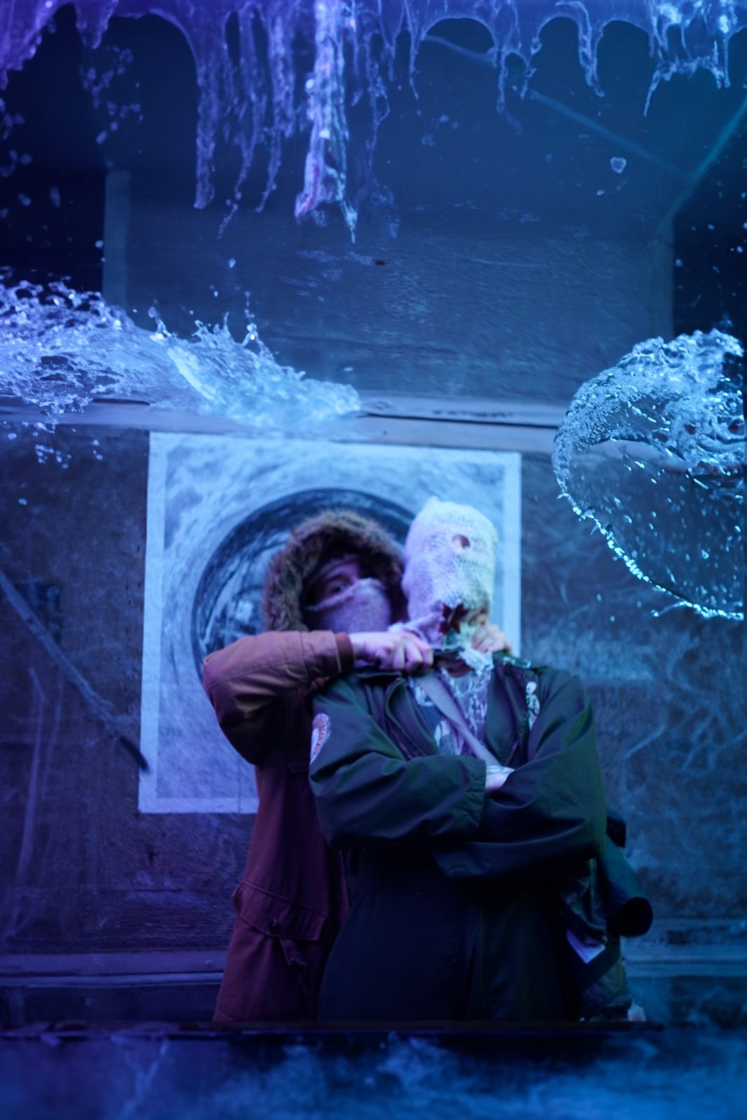 Music video still — artist lit blue beside crashing water