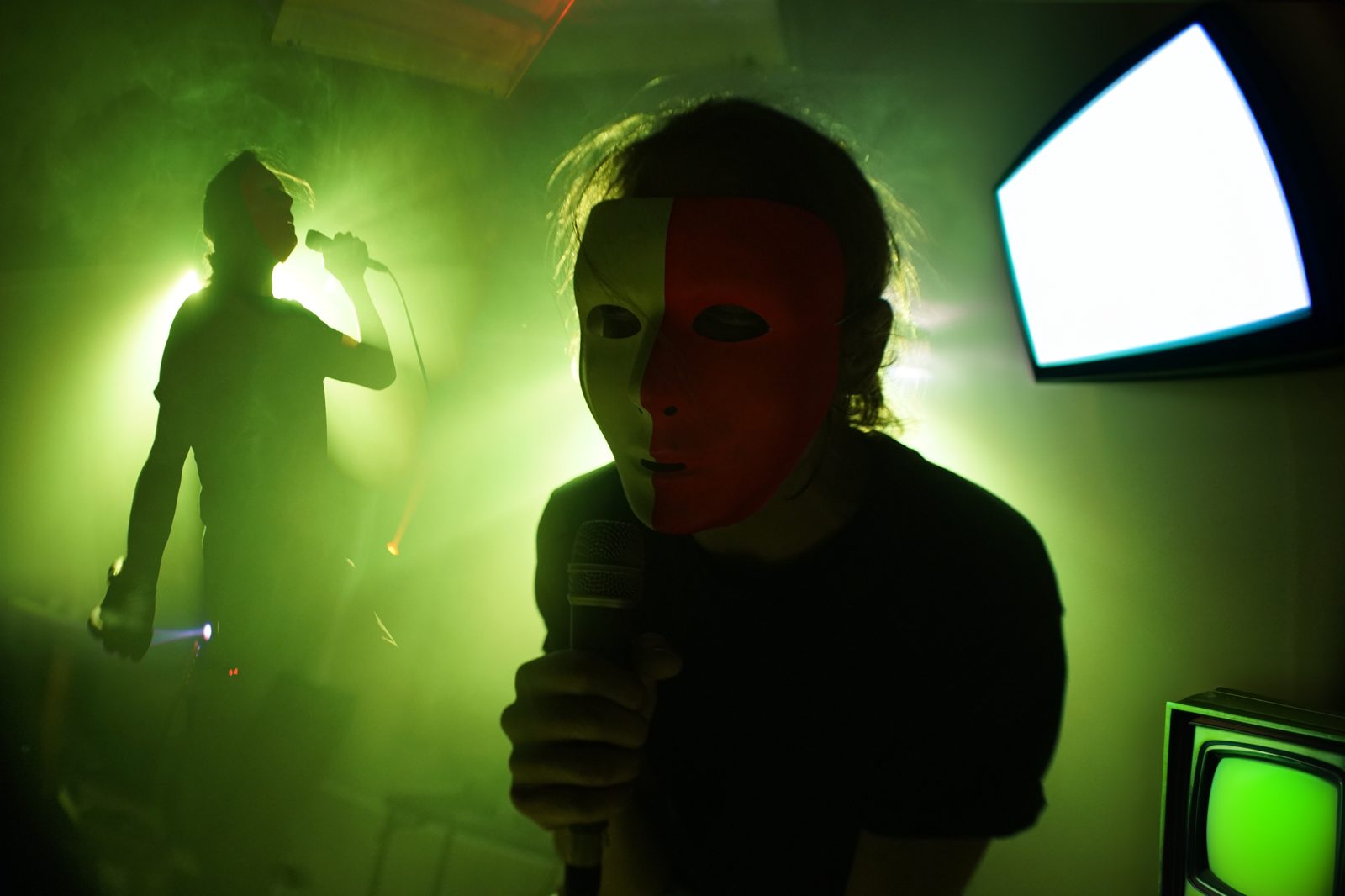 Masked performer in green fog holding a mic